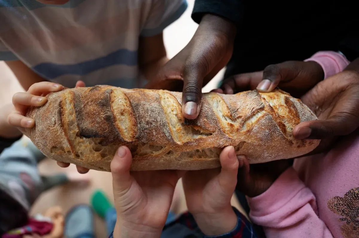 Children’s and adults’ hands hold a loaf of bread together.